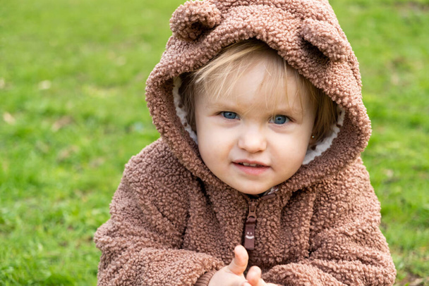 Porträt eines eineinhalbjährigen blauäugigen Mädchens im Bärenkostüm in einem Park im Gras. - Foto, Bild