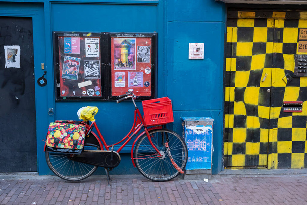 Amsterdam, Holandia - 6 września 2022 r.: Czerwony rower zaparkowany przy niebieskiej ścianie - Zdjęcie, obraz