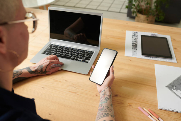 Крупним планом жінка читає повідомлення на своєму смартфоні, працюючи на ноутбуці на своєму робочому місці
 - Фото, зображення