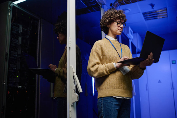 Молодая женщина-инженер концентрируется на работе по изучению данных о ноутбуке, стоящем в серверной - Фото, изображение
