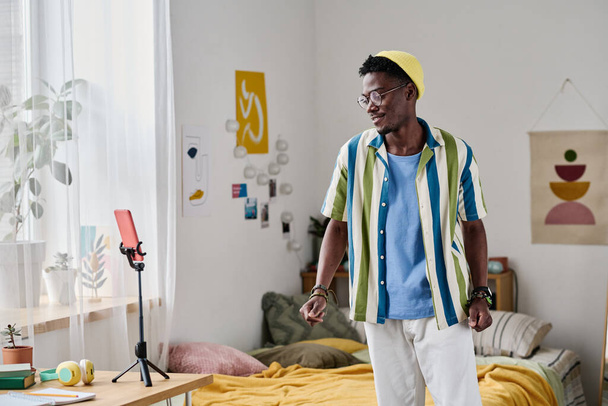 Africano adolescente grabación blog en su teléfono inteligente mientras está de pie en el dormitorio - Foto, Imagen