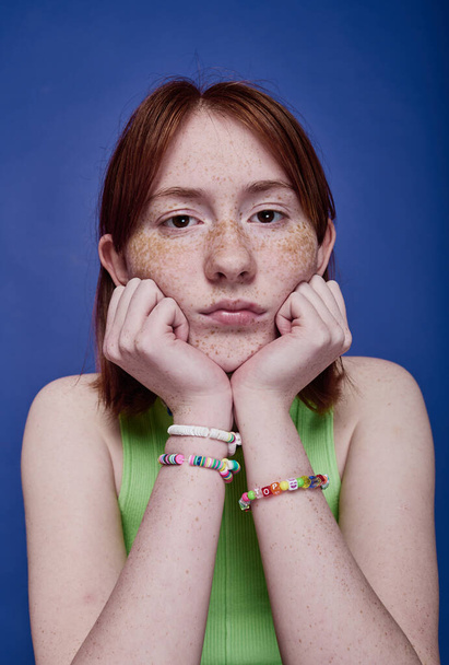 Retrato de vermelho peludo adolescente com pulseiras artesanais em seus braços olhando para a câmera no fundo azul - Foto, Imagem
