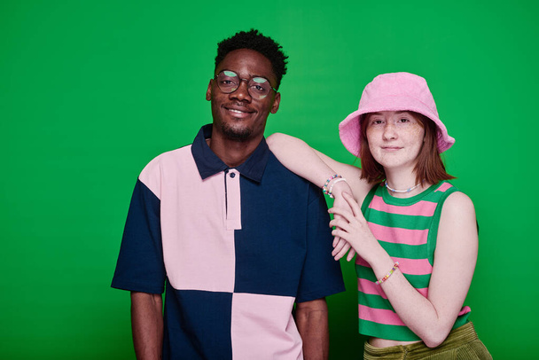 Portret van stijlvolle multi-etnische tiener paar in mode kleding glimlachen op camera poseren tegen groene achtergrond - Foto, afbeelding