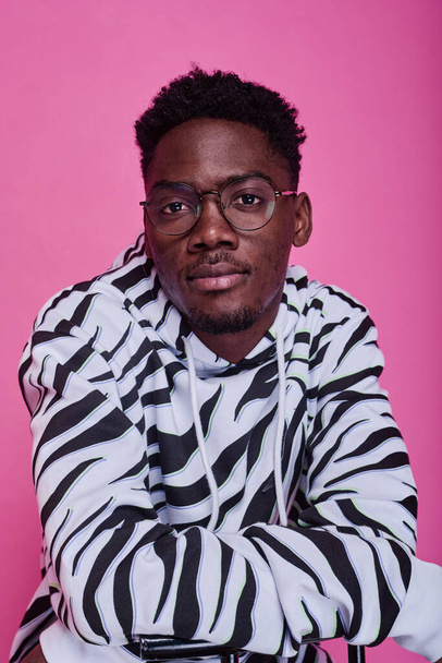 Portrait of African teenage boy in stylish hoodie with zebra print looking at camera against pink background - Фото, зображення