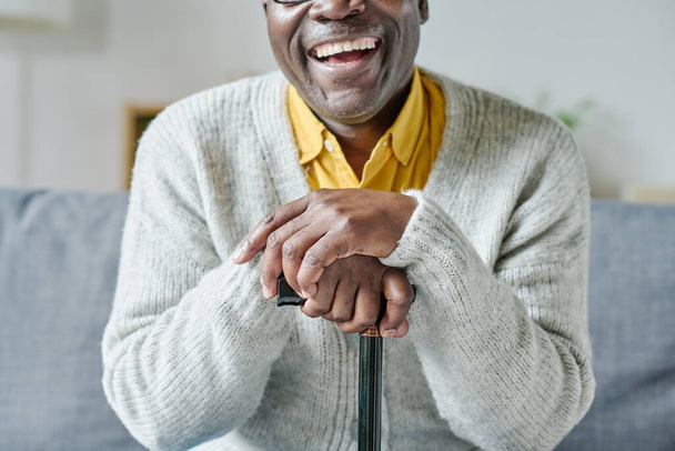 Close-up of African senior man leaning on his stick sitting on sofa and smiling - Photo, Image