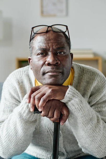 Портрет африканського зрілого чоловіка, який спирається на палицю, відпочиваючи вдома і дивлячись на камеру. - Фото, зображення