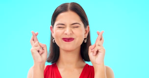 Happy, woman and face with fingers crossed on blue background, studio and wishing for good luck. Portrait of excited female model hope for winning prize, optimism and smile for emoji, hands and sign. - Footage, Video