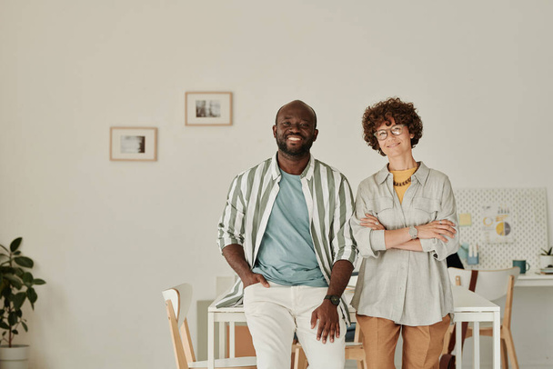 Портрет успешных молодых коллег, улыбающихся в камеру, стоя вместе в офисе - Фото, изображение