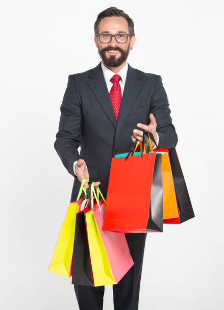40s Attractive Sales Man carrying and showing colored shopping bags isolated on white. Handsome man wearing suit and holding shopping papper bags in hands. Man shopping time for presents. - Foto, imagen