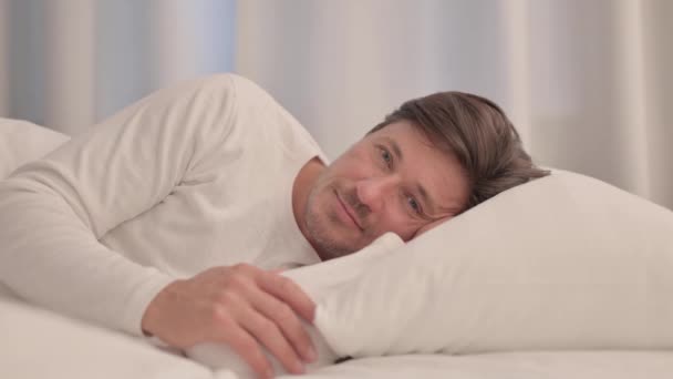 Hymyilevä kypsä aikuinen mies makaa sängyssä puolella - Materiaali, video