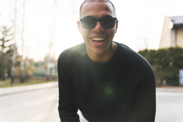 Homem afro-americano de óculos escuros sorrindo para a câmera do lado de fora na rua. Foto de alta qualidade - Foto, Imagem