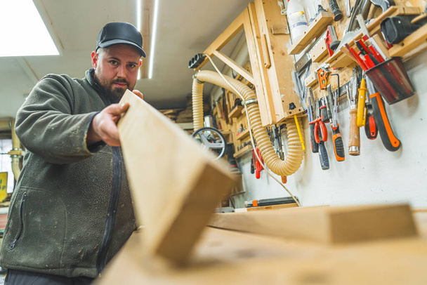 Carpinteiro profissional segurando prancha de madeira para a câmera e medindo pelo olho. Conceito de carpintaria e marcenaria. Foto de alta qualidade - Foto, Imagem