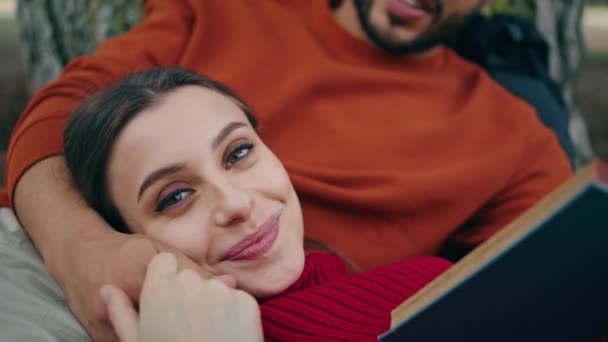 Attractive tranquil woman lying on man chest enjoying romantic picnic close up. Bearded boyfriend reading book aloud for relaxed girlfriend on nature. Cute happy couple relaxing at weekend in park. - Footage, Video