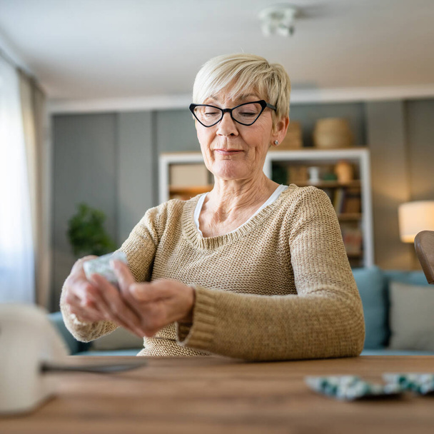 Uma mulher caucasiana sênior velha do sexo feminino tomar medicamentos ou suplemento de vitamina em casa conceito de cuidados de saúde pessoas reais - Foto, Imagem