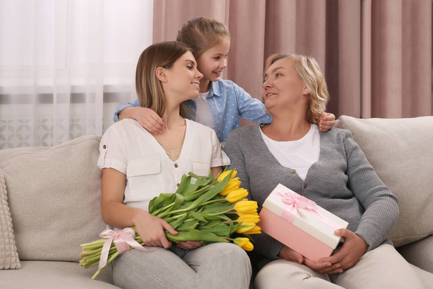 Little girl congratulating her mom and granny with flowers and gift at home. Happy Mother's Day - Фото, зображення