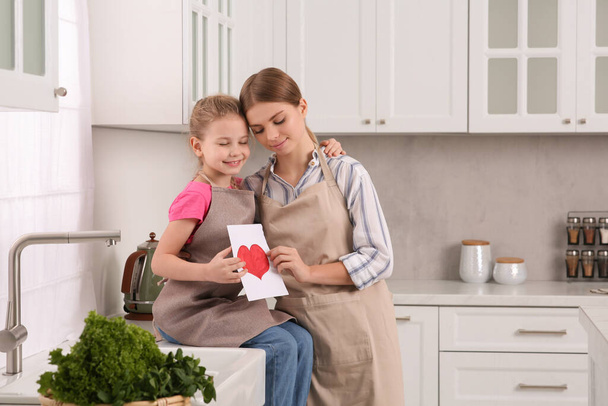 Little daughter congratulating mom with greeting card in kitchen. Happy Mother's Day - Foto, Bild