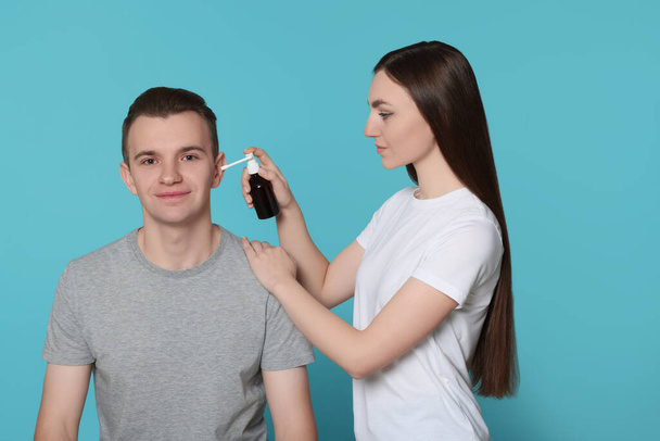 Woman spraying medication into man's ear on light blue background - Foto, afbeelding