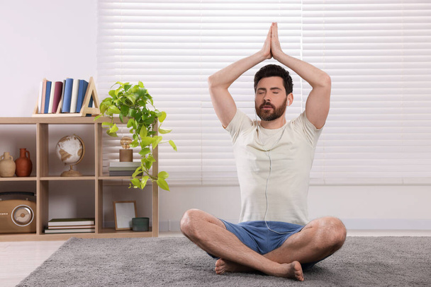 Man in earphones meditating at home, space for text - Φωτογραφία, εικόνα