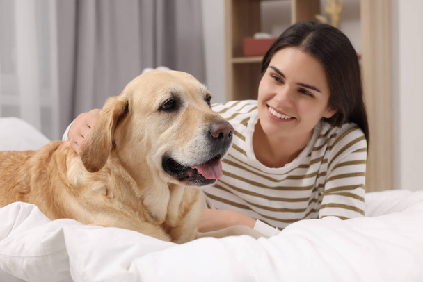 Happy woman with cute Labrador Retriever on bed at home - Fotoğraf, Görsel