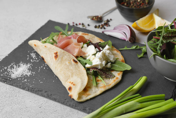 Delicious pita wrap with jamon, cheese cream and greens on light gray table - Photo, image