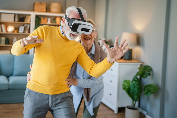 man mature senior caucasian male husband with his wife senior couple at home enjoy virtual reality VR headset - 写真・画像