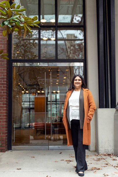 Full-length portrait of confident mature Asian woman in stylish casual clothes, smiling looking at camera, standing against a modern loft urban building background. People and lifestyles concept. - Zdjęcie, obraz