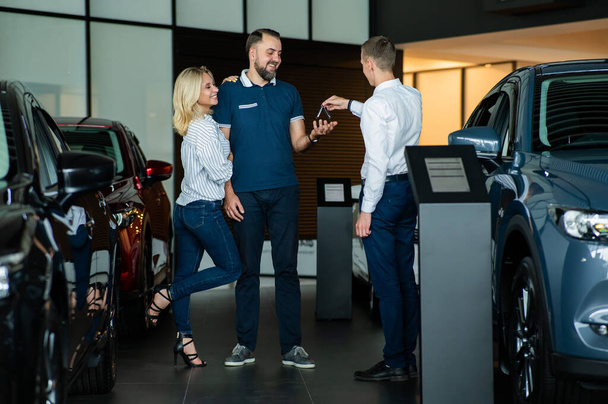 The seller hands over the car keys to the buyers. The couple bought a new car - Valokuva, kuva