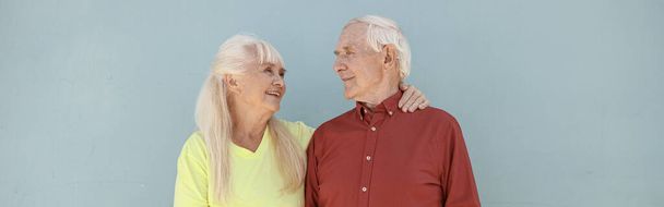 Happy positive senior woman and loving man hug standing on light grey background in studio. Love and family relationship - Foto, imagen