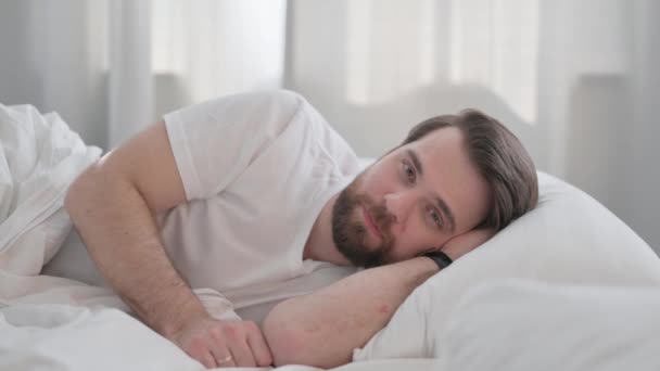 Mladý dospělý muž dělá video chat při ležení v posteli na boku - Záběry, video