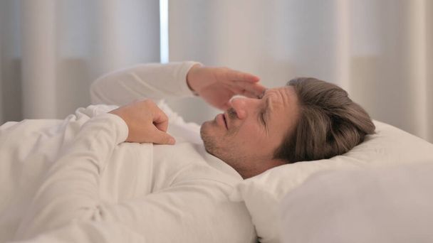 Πλευρική άποψη του ώριμου ενήλικα άνδρα με πονοκέφαλο στο κρεβάτι - Φωτογραφία, εικόνα