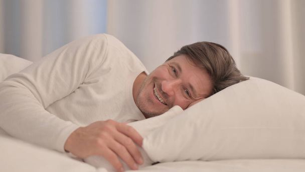 Усміхнений зрілий дорослий чоловік лежить в ліжку на боці
 - Фото, зображення