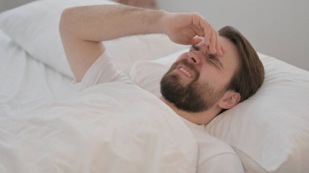 Молодий дорослий чоловік з головним болем лежить в ліжку
 - Фото, зображення