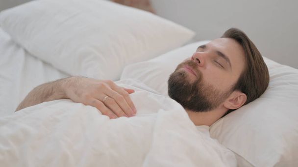 Уставший взрослый мужчина лежит в постели и спит - Фото, изображение