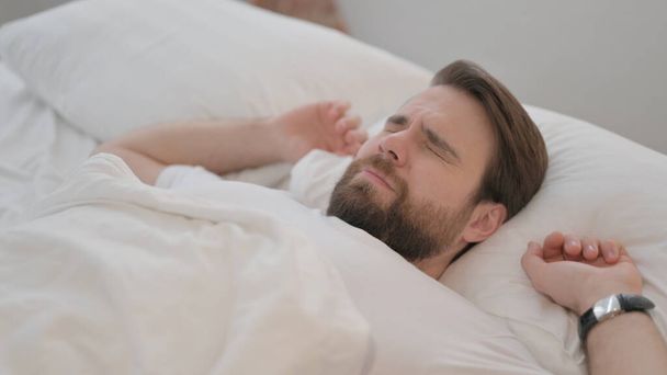 Jonge volwassen man wakker worden en verlaten van bed - Foto, afbeelding
