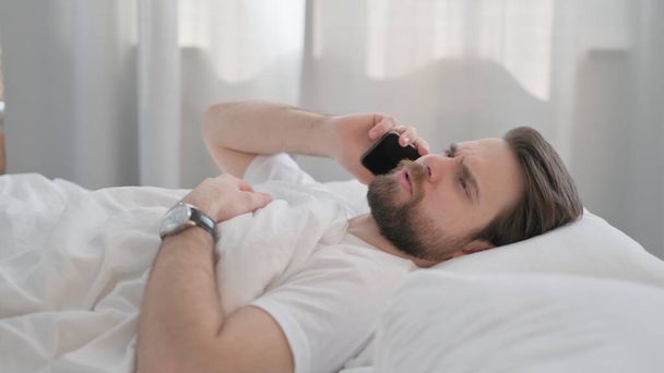 Widok z boku Młody Dorosły Mężczyzna rozmawiający przez telefon w łóżku - Zdjęcie, obraz