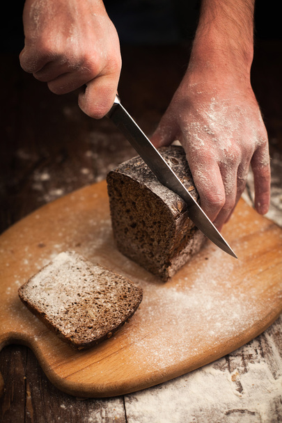 Male hands slicing fresh bread on table - 写真・画像