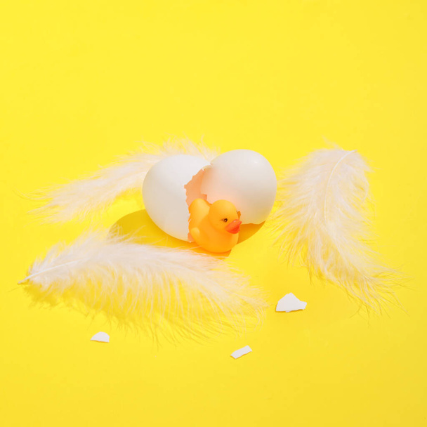 Kreatív elrendezés tojásból és tollakból kikelt kiskacsákkal. Élénk sárga háttér árnyékkal. Vizuális trend. Minimalista esztétikai csendélet. Friss ötlet - Fotó, kép