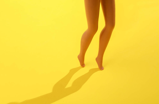 Κούκλα πόδια σε κίτρινο φόντο με σκιά - Φωτογραφία, εικόνα