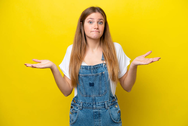 Young caucasian woman isolated on yellow background making doubts gesture - Fotoğraf, Görsel