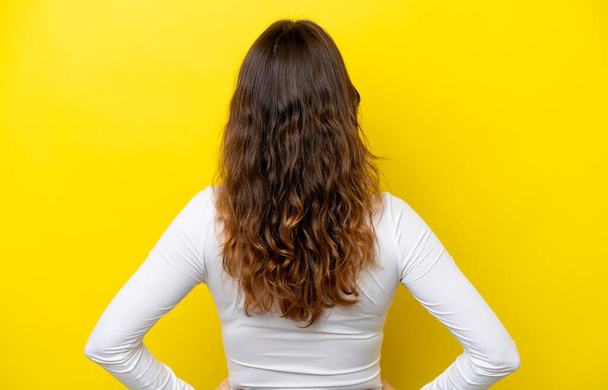 Молода біла жінка ізольована на жовтому тлі в положенні спини
 - Фото, зображення