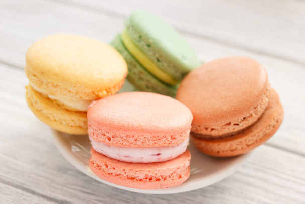Macaroons closeup on plate. Four colorful macaroon cookies on white wooden background - Zdjęcie, obraz