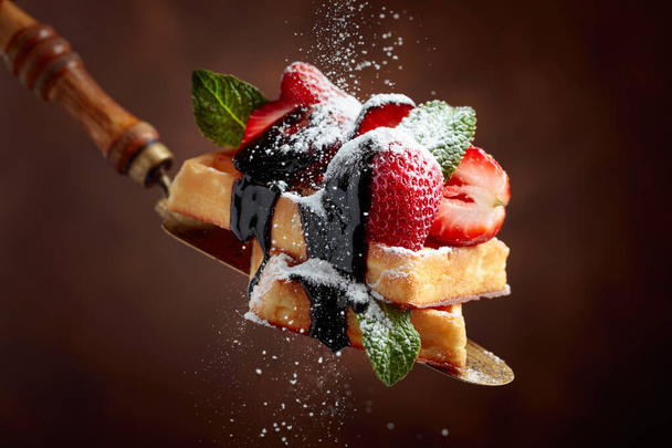 Belgian waffles with strawberries, mint and chocolate sauce, sprinkled with powdered sugar. - Photo, Image
