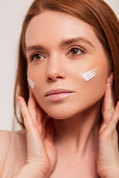 Beautiful young fresh redhead scandinavian woman with cream on face skin in studio. Beauty and skin care - Photo, Image