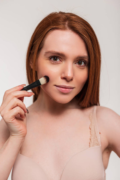 Schöne junge stilvolle Frau Rotschopf-Modell mit sauberem Gesicht Haut hält Make-up-Pinsel. Schönheit und Hautpflege - Foto, Bild