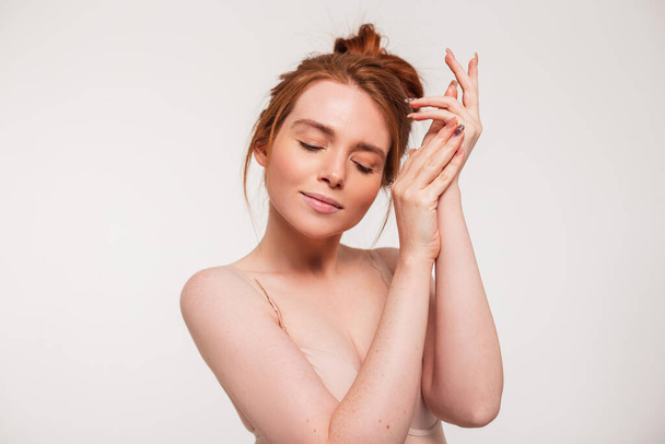 Beautiful tender young fresh girl model with red hair does hand and skin care on a white background in the studio. Beauty, health and skin care - Foto, Bild