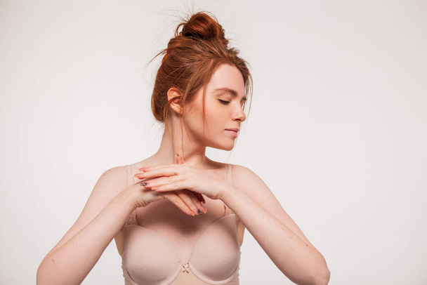 Fashion beautiful redhead fresh natural woman with clean skin in beige bra doing hand care and moisturizing with cream. Beauty and skin care - Photo, Image