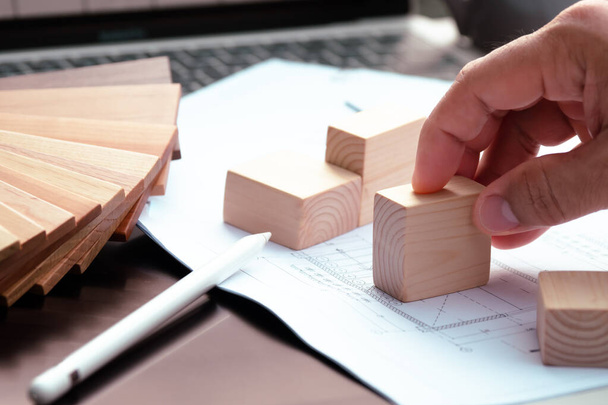 Een ontwerper legt een stuk tekenpapier op een computertafel met een blok hout erop. Het idee is om materialen voor huis decor te kiezen, en er is hout dat wordt gebruikt als een kleurenmonster. - Foto, afbeelding