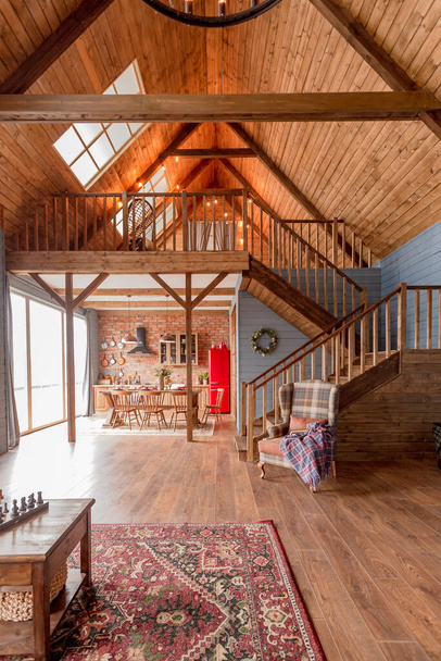 cozy all wooden interior of a country house in a wooden design. spacious living room with kitchen area with large windows. bedroom on the second floor. - Fotografie, Obrázek