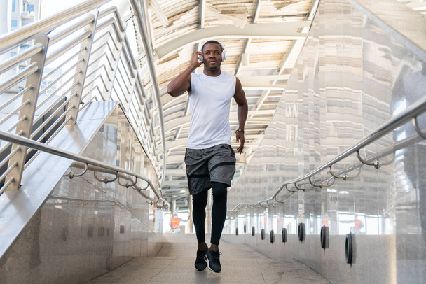 Αφροαμερικάνος με αθλητικά να τρέχει έξω στην πρωινή πόλη. νεαρός άνδρας δρομέας άσκηση τζόκινγκ δράση άθλημα, ισχυρό πρόσωπο αθλητικό. έννοια της υγειονομικής περίθαλψης. - Φωτογραφία, εικόνα