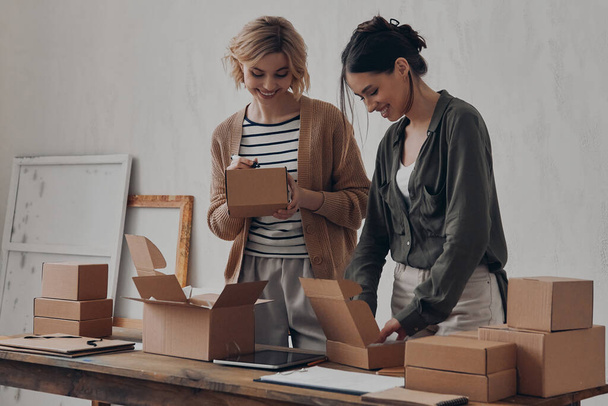 Two attractive young businesswomen preparing packages for delivery in warehouse together - Fotó, kép